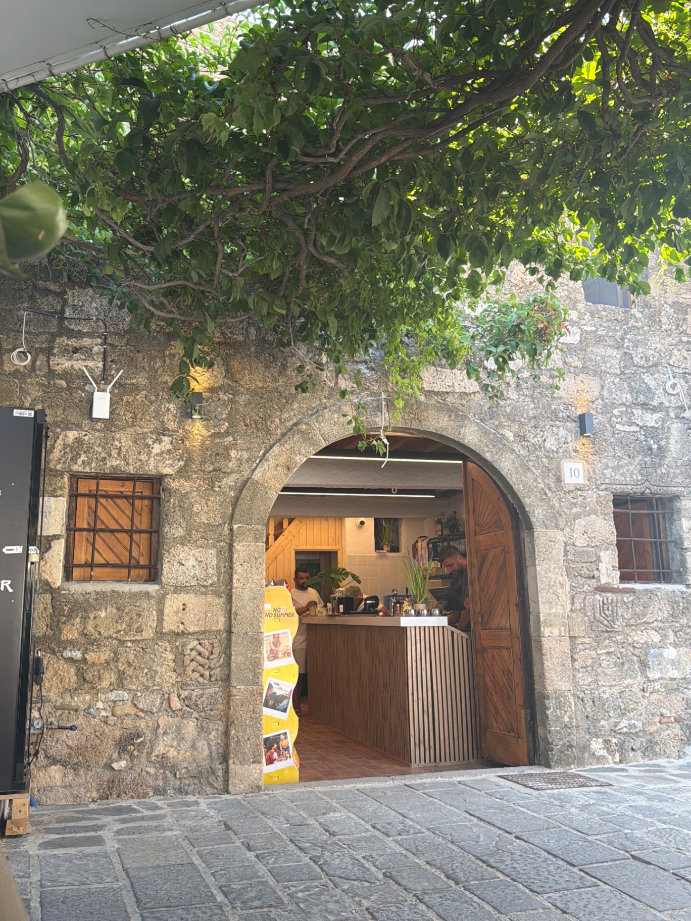 The arched stone entrance of Lindos Boathouse beneath a mulberry tree on Pallas Beach