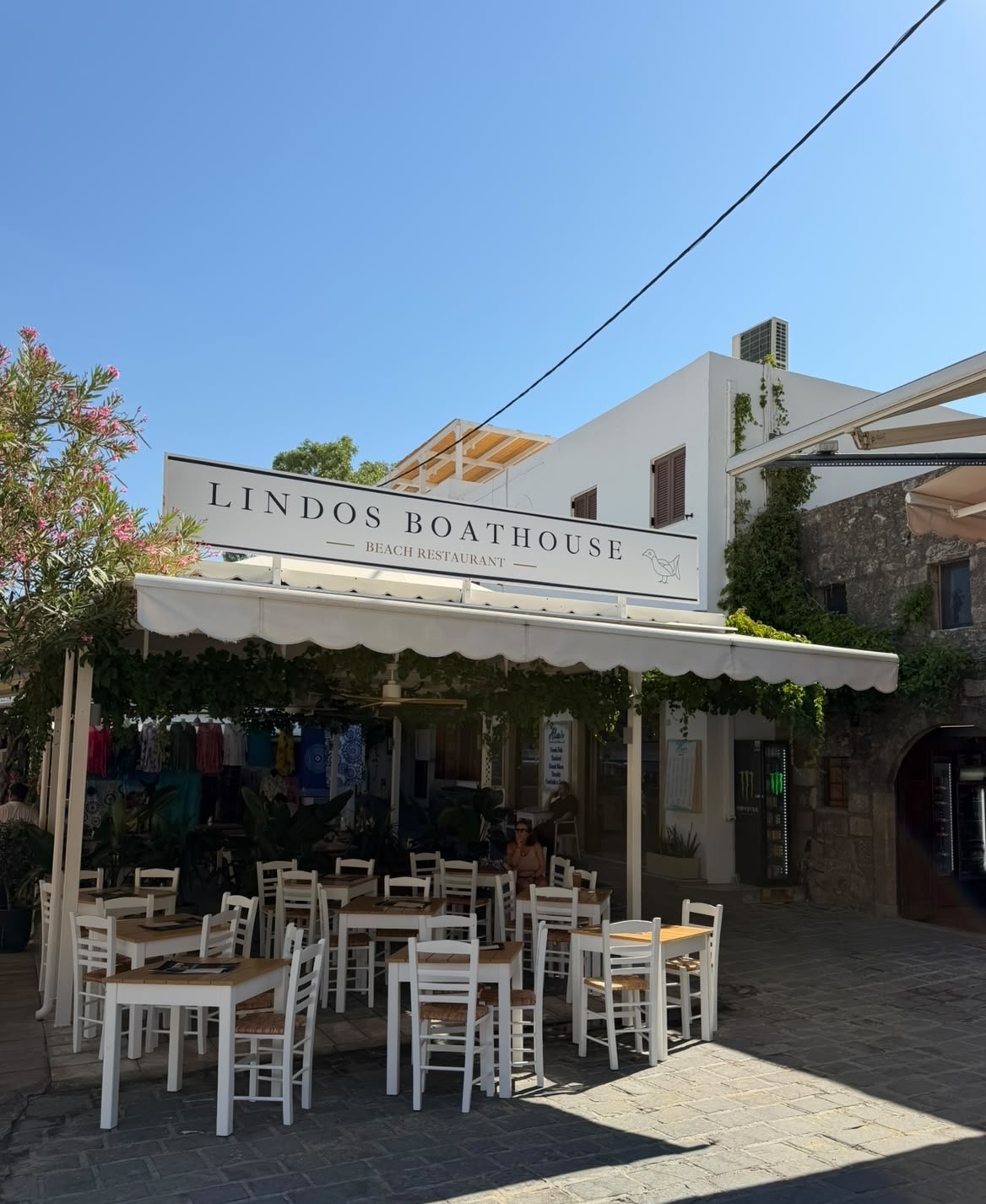 Lindos Boathouse vandaag: het bord, de luifel en de gedekte tafels onder de blauwe lucht